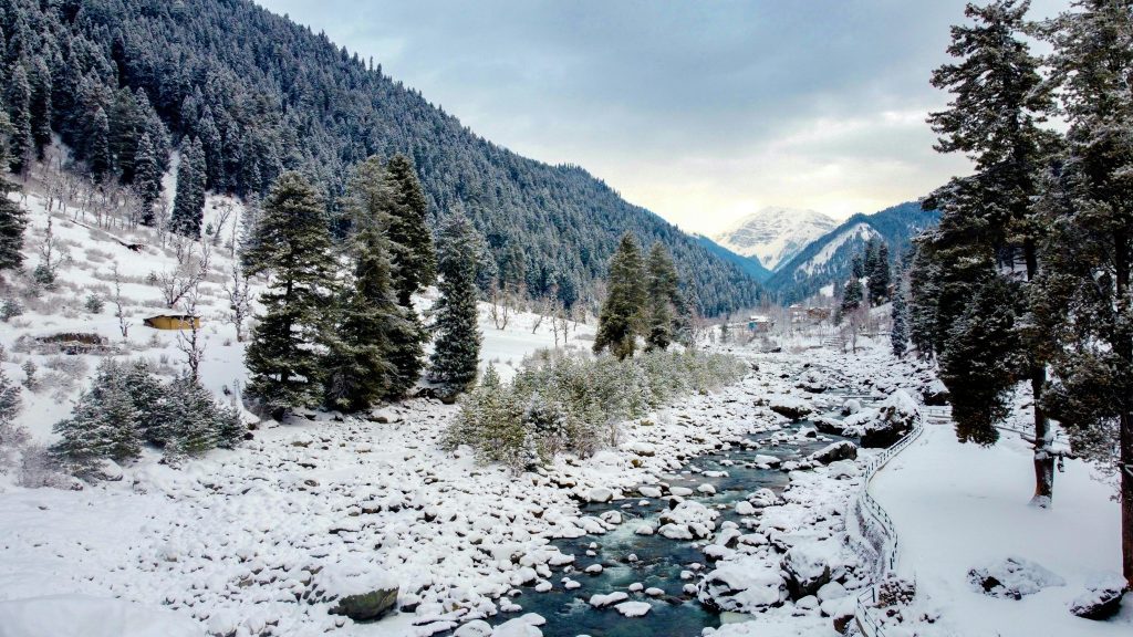 Snow covered mountain valley with river and pine trees